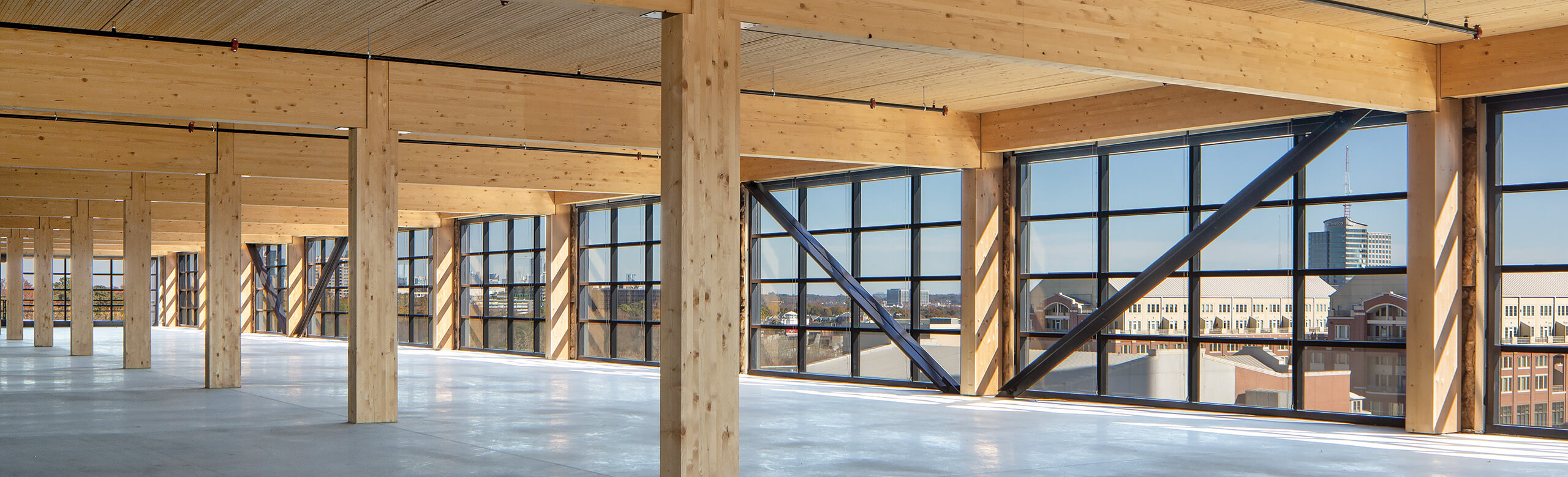 View of a newly constructed building, featuring mass timber construction and concrete flors, overlooking a city skyline.